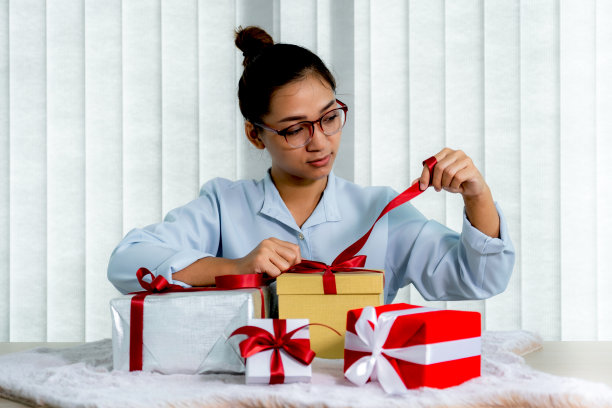 女人手里拿着一件蓝色衬衫打开一个用红丝带绑着的金礼盒，礼物是为圣诞节、情人节等特殊节日赠送的图片下载