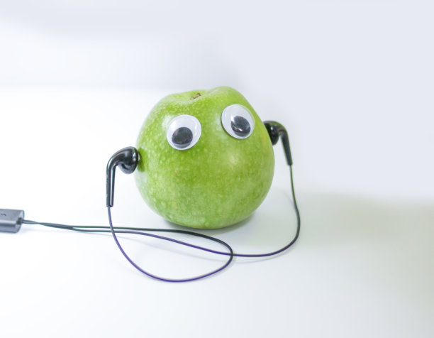 绿色的小苹果，可爱的眼睛和耳机在白色的背景。概念上的照片。图片下载