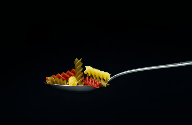 干燥的螺旋意大利面在一个银色金属勺子孤立在黑暗的背景变化。意大利食物，碳水化合物营养概念。图片下载