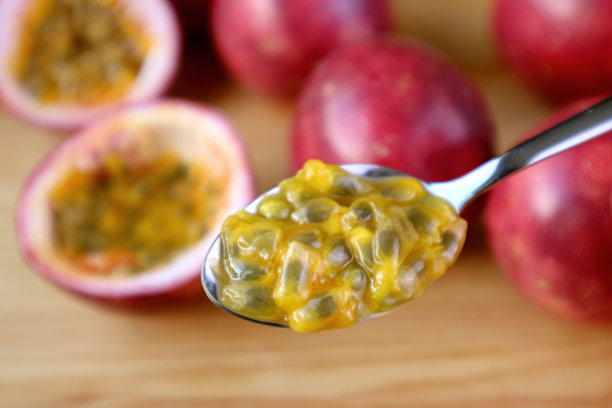 近距离的果肉和种子的成熟的百香果勺子上模糊的整个水果在背景图片下载