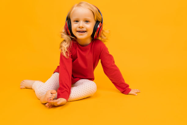小女孩坐在地板上，用耳机听黄色背景的音乐图片下载