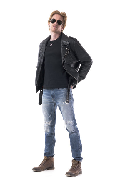 一个自信的摩托车手，穿着皮夹克，戴着墨镜，穿着靴子，双手插在后面的口袋里图片下载