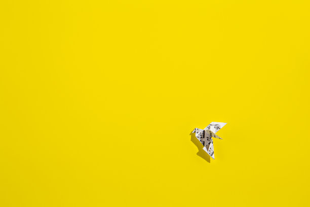 在黄色背景上飞翔的折纸鸽子。图片下载