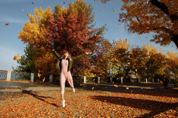 一个女人在秋叶中快乐地跳着。图片下载