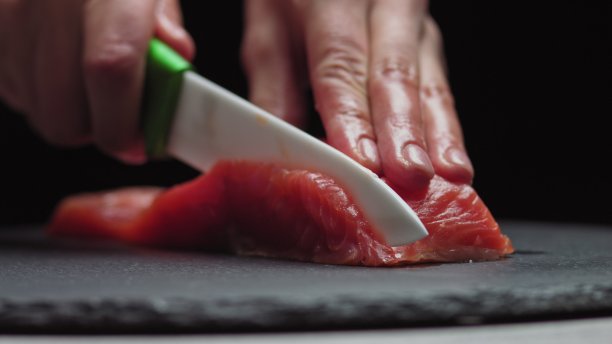 寿司师傅在寿司吧切新鲜的鲑鱼。厨师在专业厨房切三文鱼片。特写厨师用手在慢镜头中切鲜鱼片。正在切红鱼的职业男子图片下载