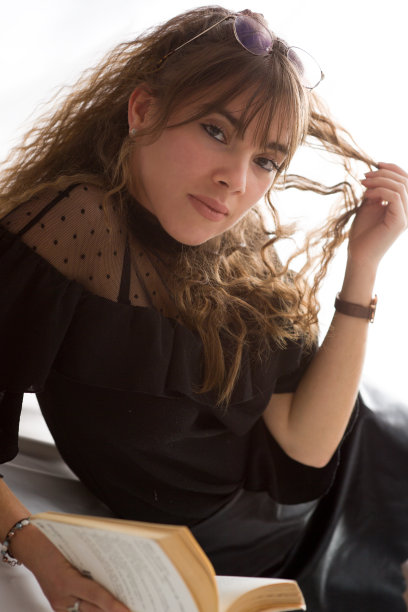 年轻女子拿着一本书，看着镜头，摸着自己的头发图片下载