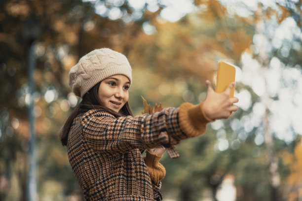 十几岁的女孩在公园里拍秋叶的照片图片下载