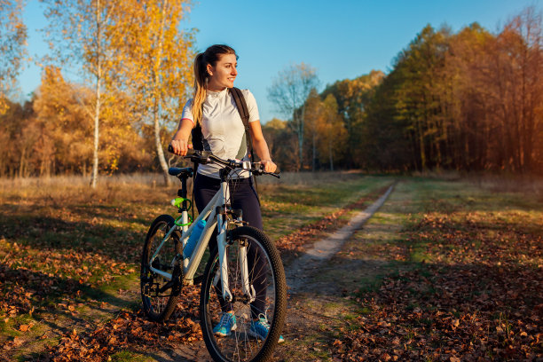 在秋天的森林里骑自行车。年轻女子在自行车上锻炼后休息，享受大自然。健康的生活方式图片下载