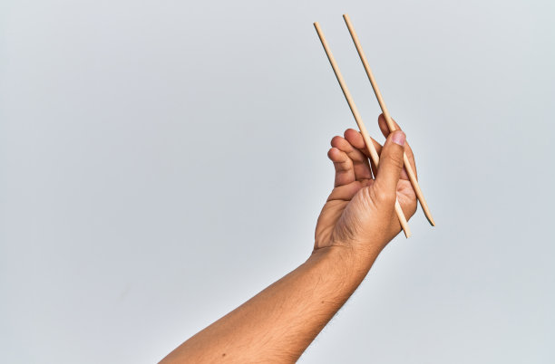 手持木筷子的西班牙人的手越过孤立的白人背景。图片下载