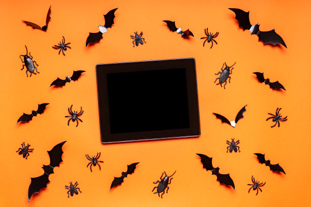 万圣节组成。橙色背景上有黑蝙蝠、蜘蛛、苍蝇和臭虫。黑色空白平板屏幕，模拟。万圣节快乐，不给糖就捣蛋的派对理念。平铺，俯视图，拷贝空间图片下载
