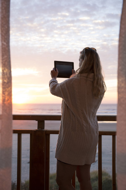 一名女子用数码平板电脑拍摄海面上的日出图片下载