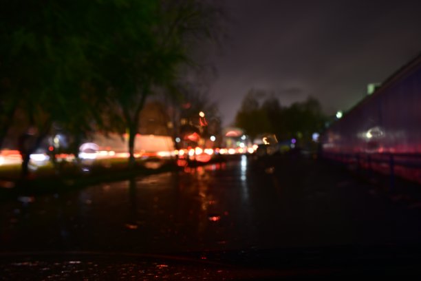 昏暗城市街道上的模糊照片。汽车前灯和雨点落在挡风玻璃上图片下载