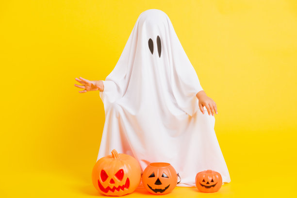 小可爱的孩子穿着白色的服装万圣节鬼吓人，他抱着橙色的南瓜鬼图片下载