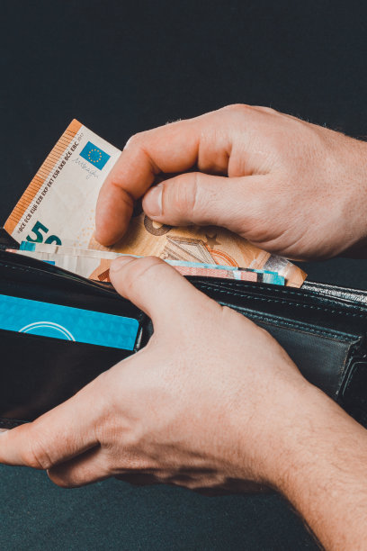 特写的人的手把欧元钞票在钱包孤立的黑色背景。图片下载