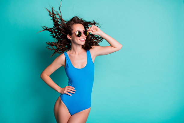 漂亮可爱可爱的苗条女士模特的照片触摸眼镜看空的空间通风的发型夏装配件商店广告概念穿蓝色泳衣孤立的绿松石色背景图片下载