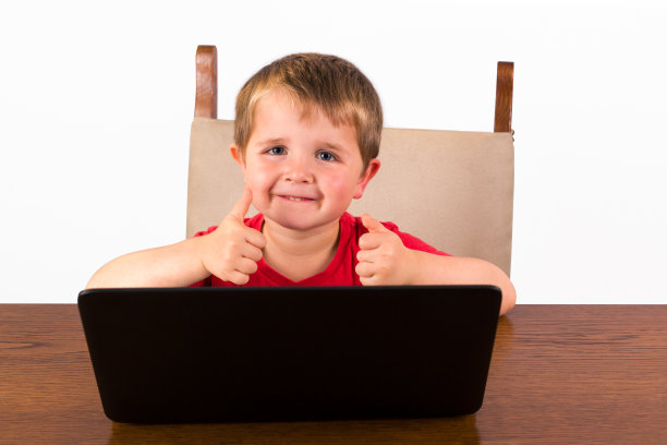 蹒跚学步的孩子坐在笔记本电脑后面竖起大拇指图片下载