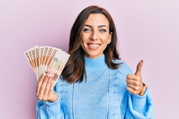 年轻的黑发女子拿着5000韩元的钞票微笑，开心和积极，大拇指做优秀和赞同的标志图片下载