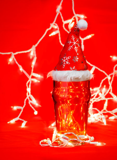 一品脱啤酒或啤酒与圣诞红帽子和灯在红色背景图片下载