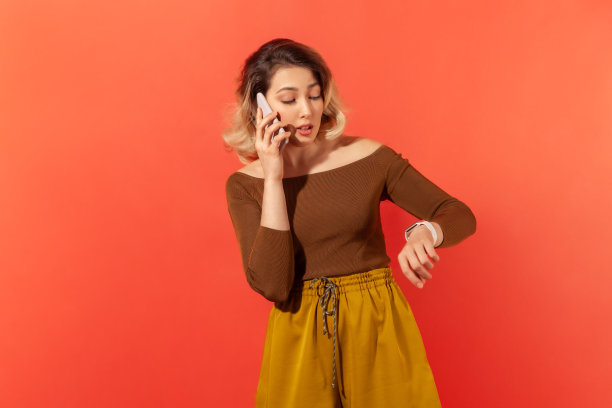 美丽的女人讲电话看手表在她的手腕，约会或约会图片下载