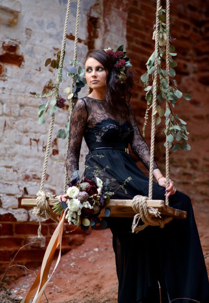 漂亮的女孩穿着黑色的裙子，头发上戴着一束鲜花，在秋千上摇摆。万圣节的概念。图片下载