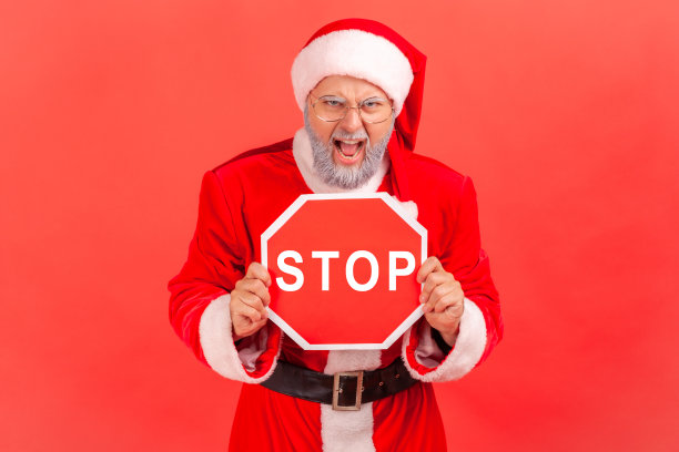 愤怒的戴着眼镜、穿着圣诞老人服装的灰胡子男子举着“停止”标志，“不行”，警告节日庆祝活动。图片下载