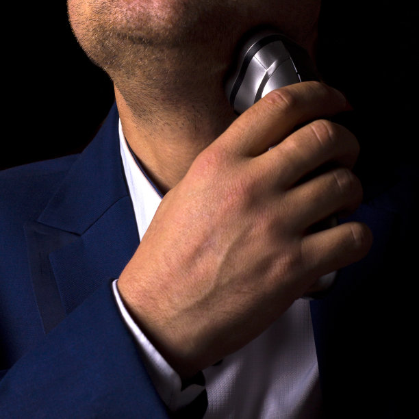 一个穿西装的男人用电动剃须刀刮胡子。为商务会议做准备。男人的日常仪式。图片下载