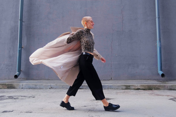 一位穿着豹纹高领毛衣、戴着红色眼镜的短发女子在城市的街道上跳舞、散步、微笑。图片下载