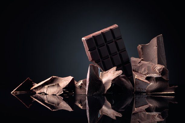 一块碎巧克力和几块黑巧克力在黑色反光的背景上。图片下载