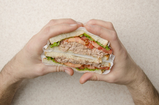 金枪鱼三明治，生菜，西红柿和洋葱，白种人的手切成两半图片下载
