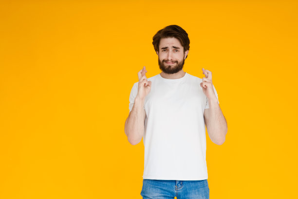 微笑的大胡子男人男人在白色休闲t恤孤立在黄色背景。人们生活方式的概念。模拟拷贝空间。等待特别的时刻，手指交叉，咬嘴唇，许愿图片下载