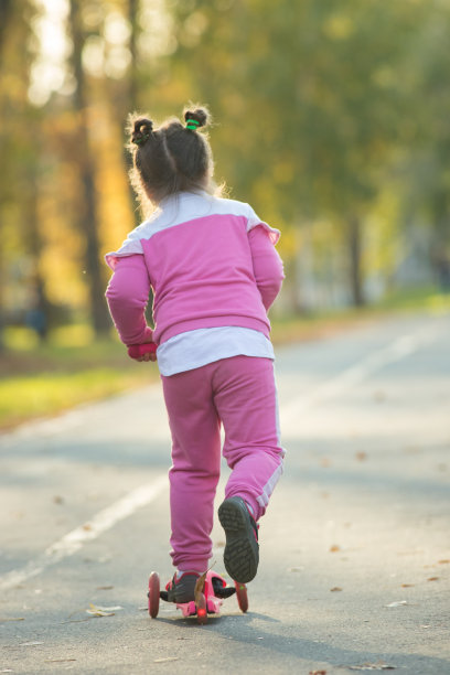 一个穿着粉色服装的小女孩在秋天的公园里骑着小型摩托车图片下载