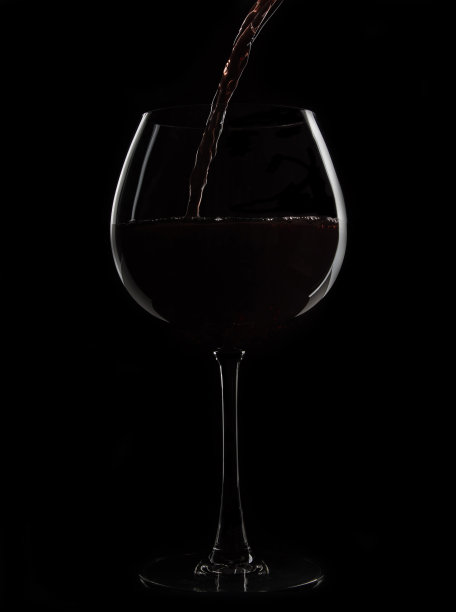 黑色背景上倒着红酒的杯子。玻璃的边缘被灯光照亮。图片下载