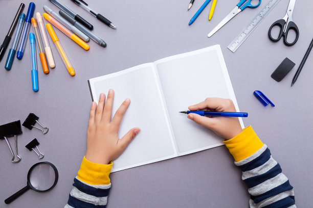 教育的概念。一个男孩手里拿着一支蓝色的钢笔，一个打开的格子笔记本和各种文具。图片下载