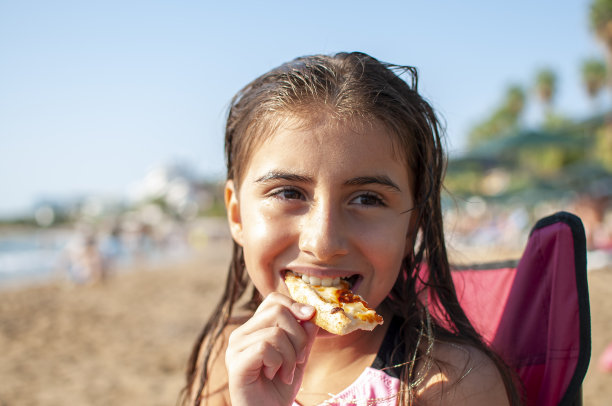 一个小女孩吃着披萨去海滩图片下载