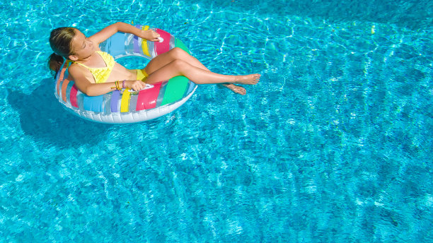 活泼的女孩在游泳池空中俯瞰，孩子在充气圈上游泳，孩子在家庭度假胜地的蓝色海水中玩耍图片下载