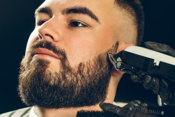 理发店的客户。一个男人正在用电动剃须刀修剪他的胡子图片下载