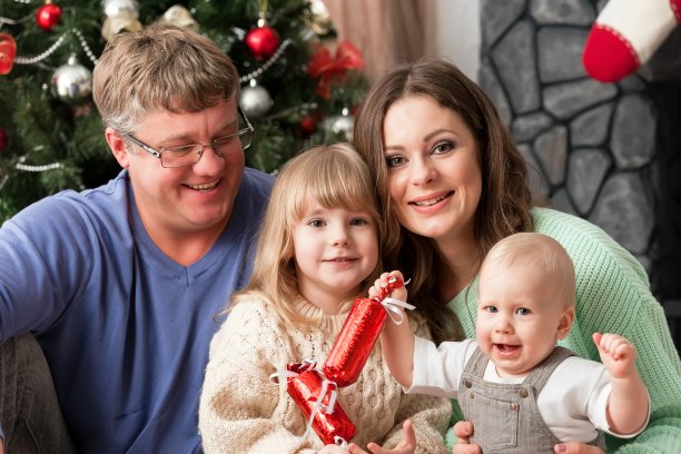 一个年轻的家庭和孩子在家里的新年前夕的壁炉和靠近圣诞树图片下载