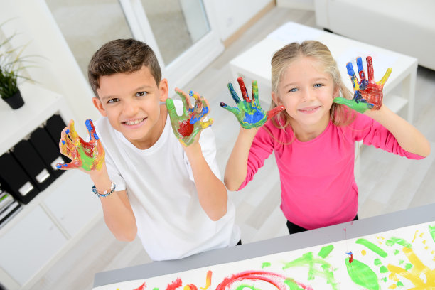 两个漂亮的小男孩和女孩用彩色颜料在白纸上手绘图片下载