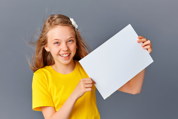 一个十几岁的女孩穿着黄色的衣服，灰色的背景拿着一个空白的白色海报的概念插入图片下载