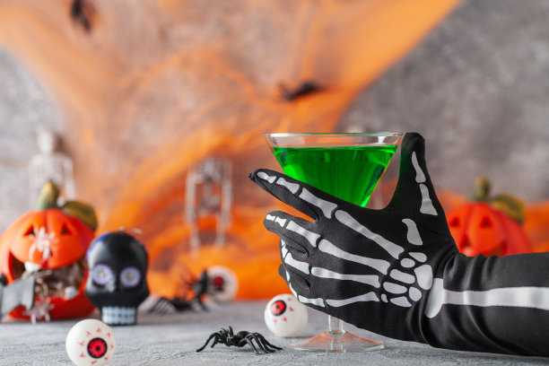 万圣节喝绿色鸡尾酒马提尼为派对手在手套握玻璃在节日的背景。图片下载
