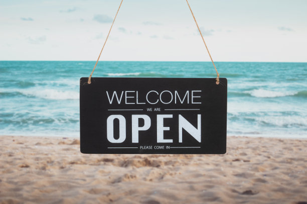 海滩上的黑色牌子上写着"请进，我们开门了图片下载