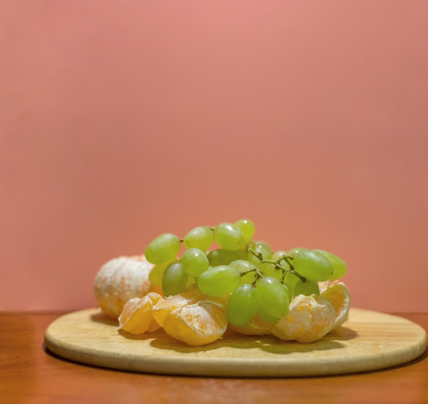 一串葡萄和桔子片放在一个木架子上，以粉红色为背景。仍然生活。副本的空间。图片下载