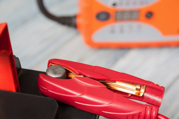 一个汽车电池与红色和黑色电池跳线夹和汽车电池充电器的背景。特写镜头,有选择性的重点图片下载