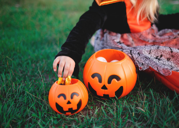 一个孩子的手伸向南瓜形状的糖果篮子里的糖果图片下载