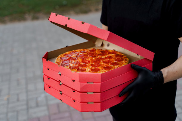 餐厅安全送披萨。食品快递在黑色医疗手套。披萨与奶酪和意大利腊肠的孤立照片。阻止冠状病毒新冠肺炎大流行图片下载