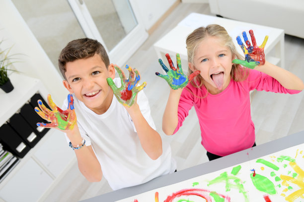 两个漂亮的小男孩和女孩用彩色颜料在白纸上手绘图片下载
