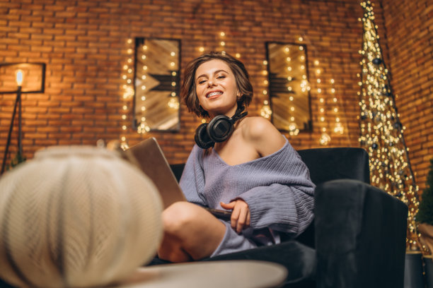 漂亮的年轻褐发女子在家里戴着耳机使用笔记本电脑图片下载