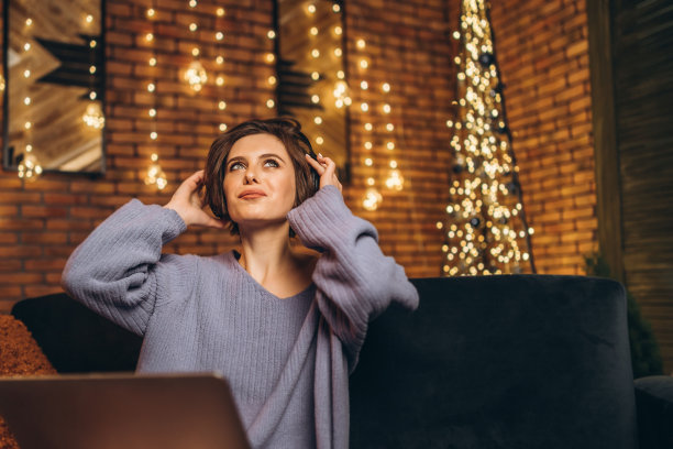 漂亮的年轻褐发女子在家里戴着耳机使用笔记本电脑图片下载