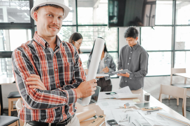 年轻的工程师戴着头盔看着照相机的蓝图在办公室，工程师的概念图片下载