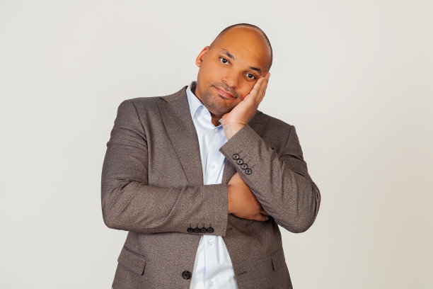 一个年轻的非洲裔美国人商人的肖像，他的手在他的脸和冷漠地盯着镜头，认为他看起来疲倦和沮丧的交叉双臂。图片下载